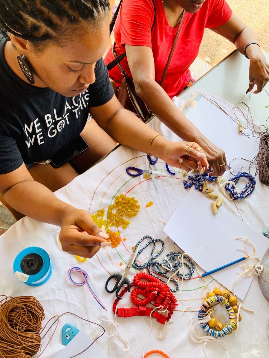Two women threading colourful beads into jewellery at a bead-making workshop in Accra
