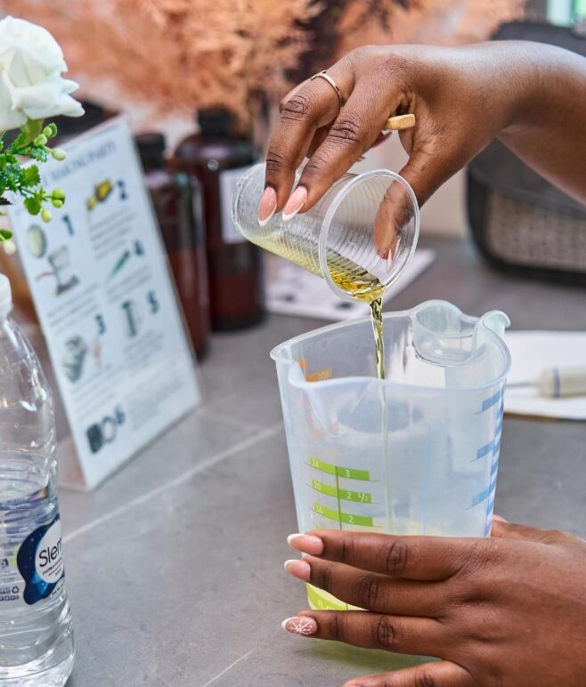 Hands pouring golden melted wax into a jug at a candle-making class in Accra