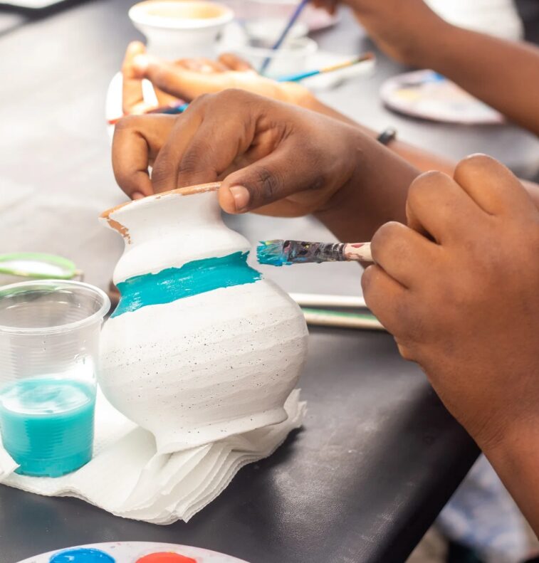 Hands painting a white ceramic vase with a blue band in Accra