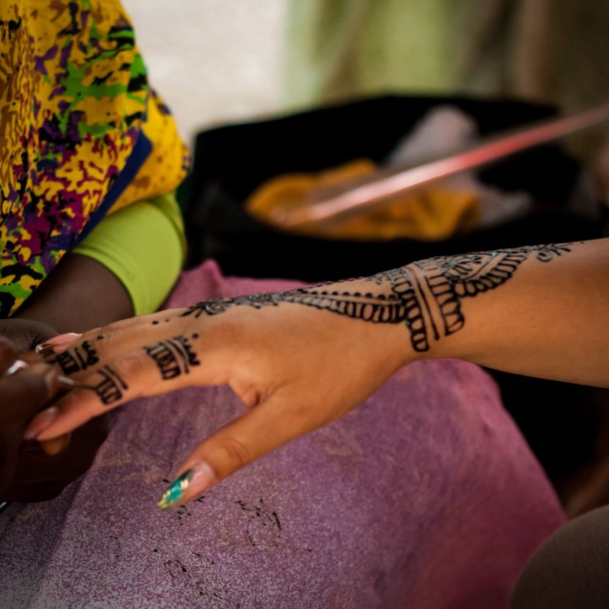 A henna cone applying a detailed pattern to a guest's hand in Accra