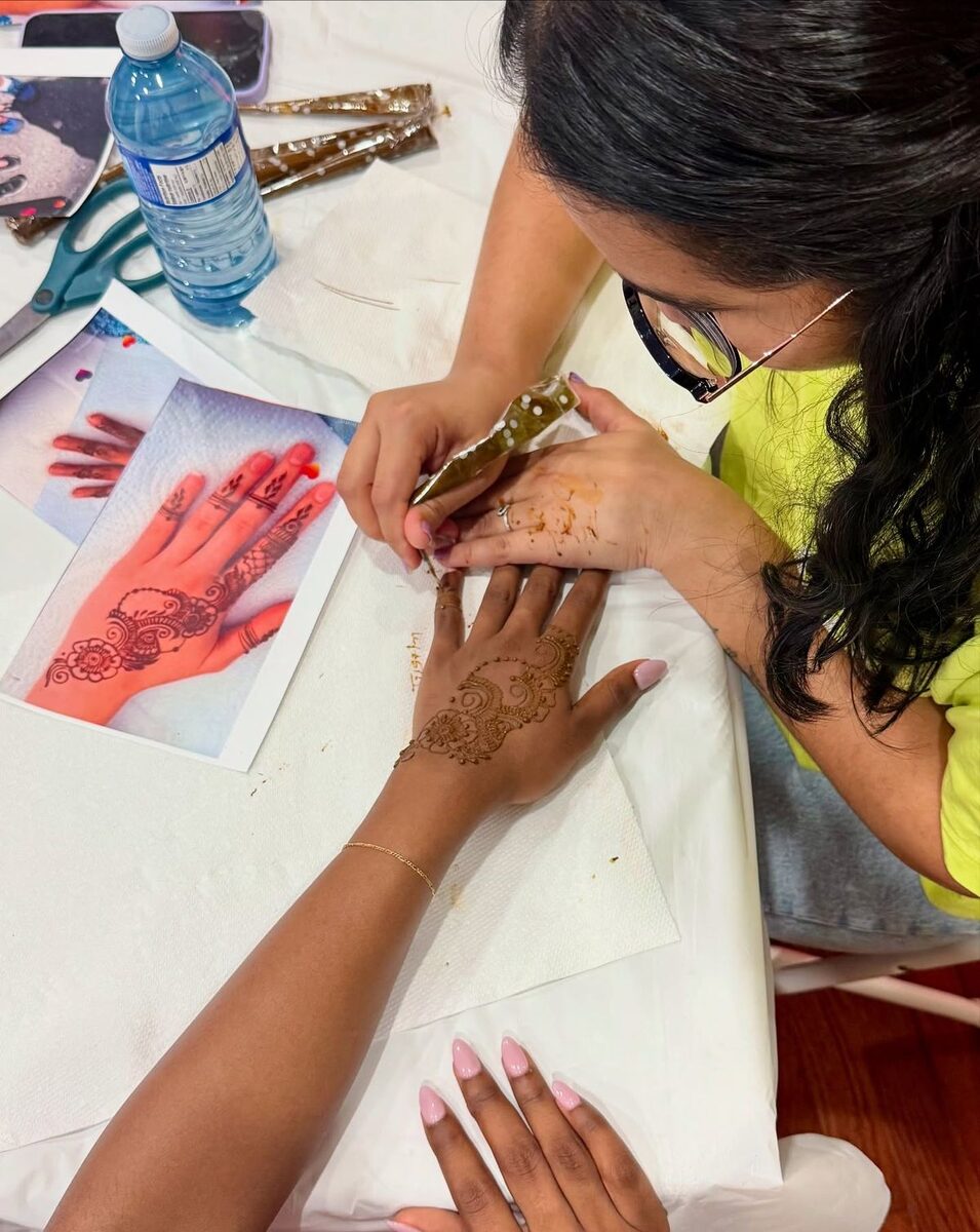 A henna artist applying a design from a reference sheet at a henna session in Accra