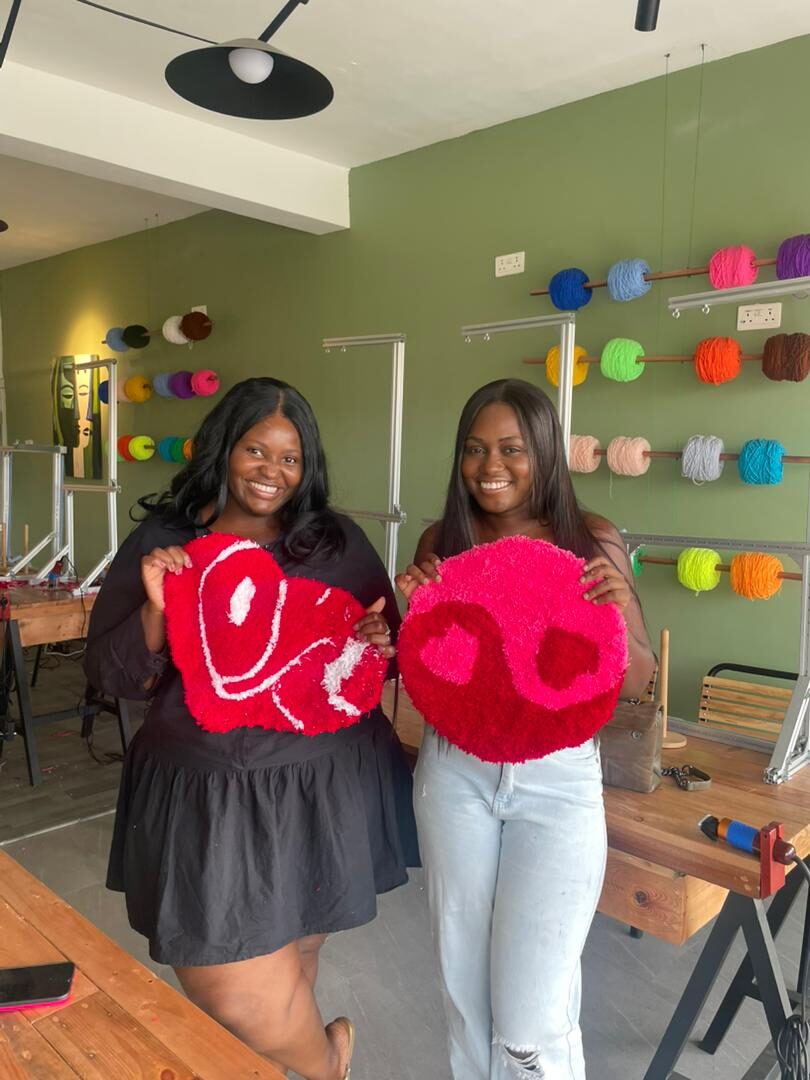 Two guests holding smiley-face tufted rugs they made at a tufting studio in Accra