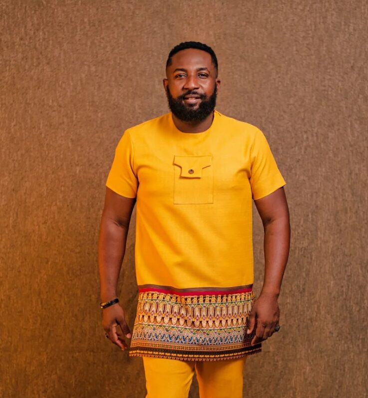 A man wearing a custom yellow African set with a kente waist wrap in Accra