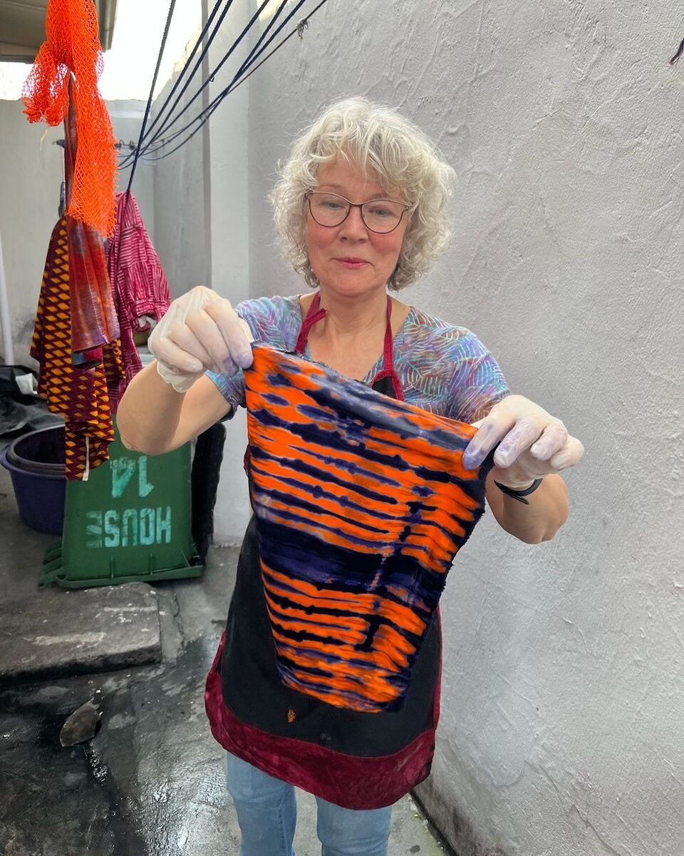 A workshop guest holding up the orange and black tie-dyed cloth she made in Accra